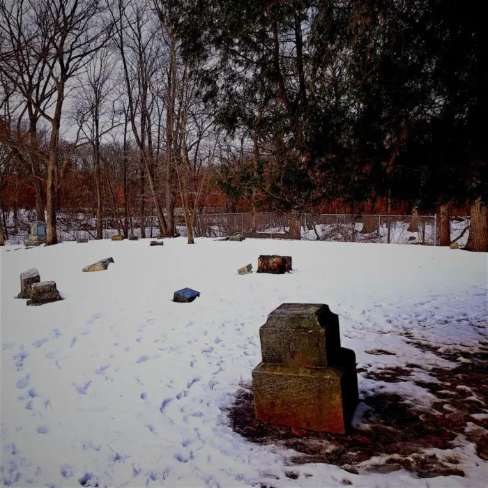 Snow covered cemetery with a scattering of gravestones all over.