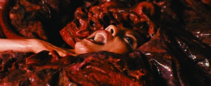 A face is seen shouting from a gory, red presence enveloping a young woman in The Seed