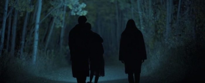 Three people walk in the woods at night guided by a flashlight