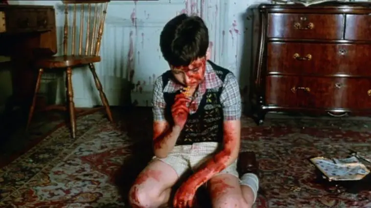 A young boy, covered in blood, kneels on the floor as he works on a jigsaw puzzle during the opening scene of the film Pieces.