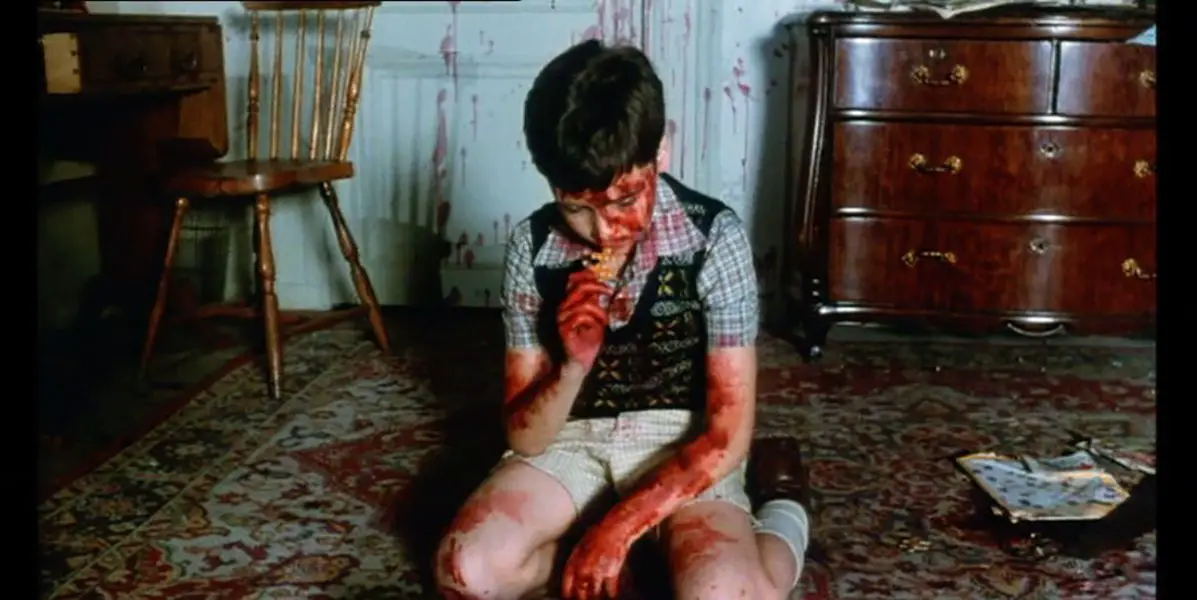 A young boy, covered in blood, kneels on the floor as he works on a jigsaw puzzle during the opening scene of the film Pieces.