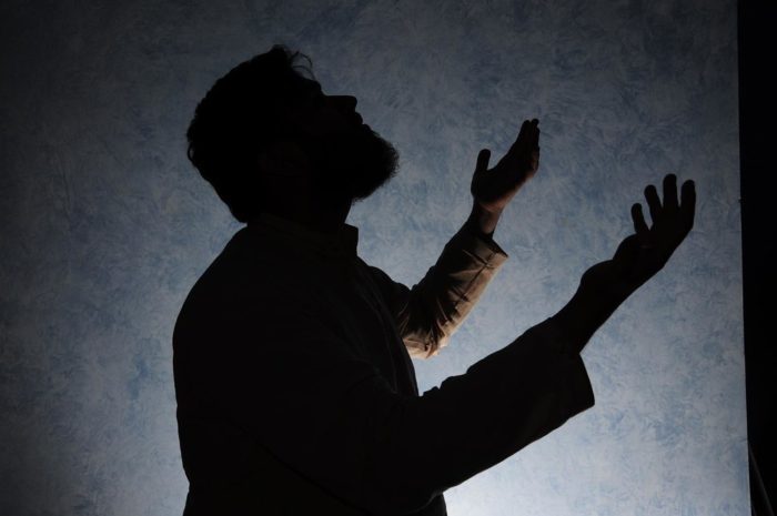A bearded man looks above with his hands offered in prayer