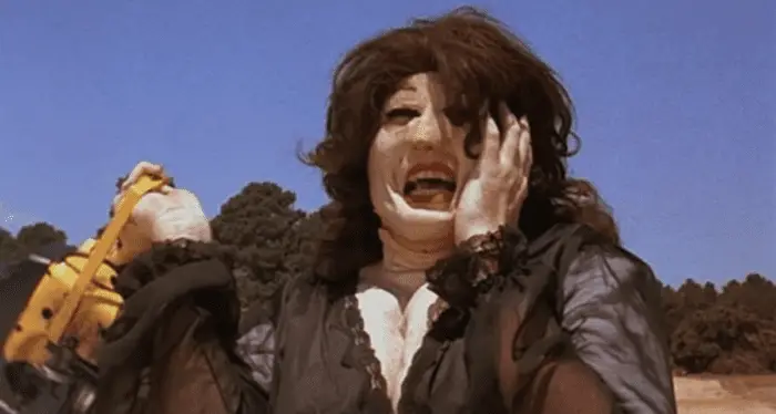 Leatherface, dressed in drag, is in a field holding a chainsaw