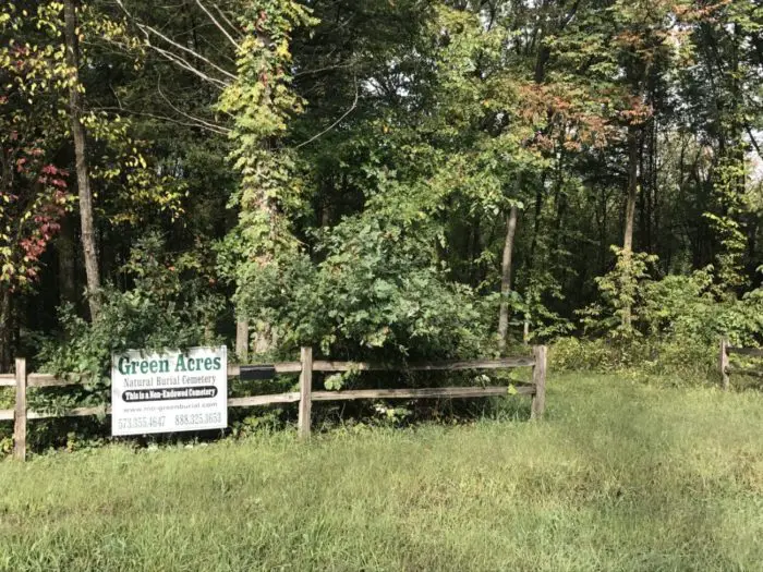 A day time shot of a wooded area with a sign that says "Green Acres Natural Burial Cemetery." .