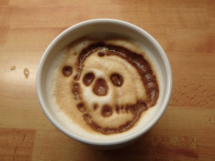 A foam skull face grins from the surface of a cup of coffee.
