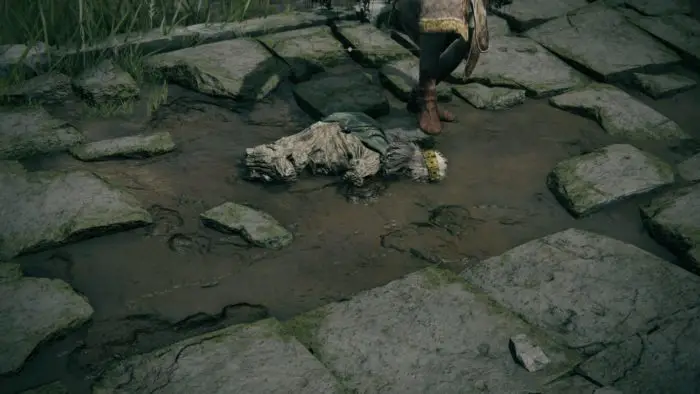 A dismembered corpse lays in the dirt, being kicked by a person off-screen