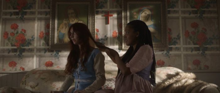 Saratoga braids Lydia's hair in front of the flowered wallpaper in Hell is Empty