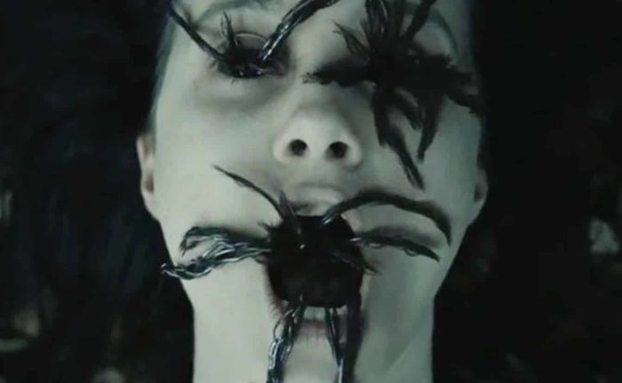 A closeup of a girl's face covered in spiders as she opens her mouth to scream.