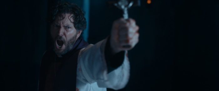 Father Peter is seen sweaty and shouting, holding up a cross in The Exorcism of God.