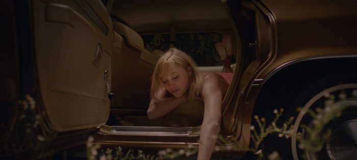 Jay leans out a car door picking at the ground in It Follows