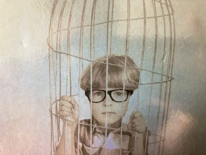 A young kid wearing glasses trapped in a bird cage