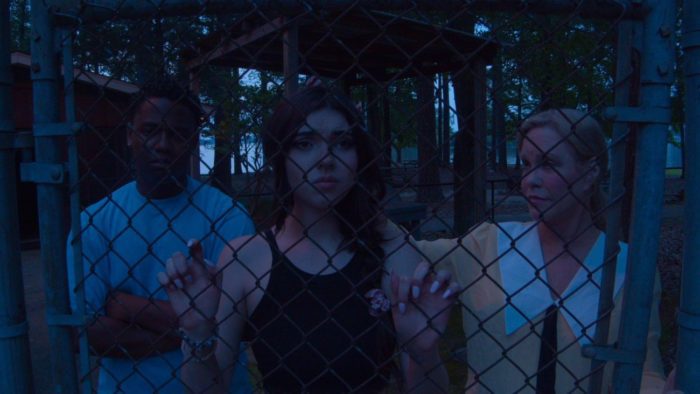 Jackson, Emma, and Mary Esther stand behind a chain linked fence in Children of Sin