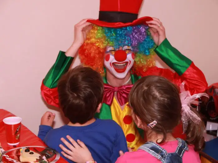 A smiling happy clown entertains a group of children.