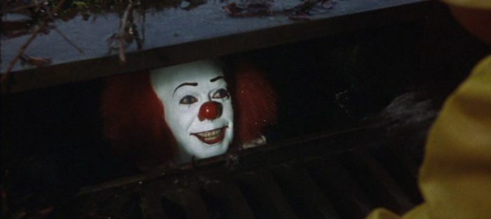 Pennywise the clown looks up from the darkness of the sewer.