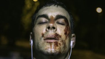 Dani is seen with his face covered in blood, wearing headphones in Cross the Line