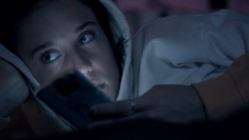 A screenshot from Ego shows Paloma (Maria Pedraza)laying in bed, idly holding her phone, lit by the light of the screen, and looking to the left