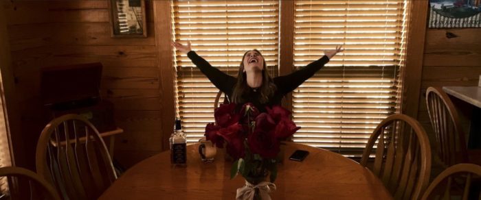 Faye extends her arms and laughs toward the sky at the kitchen table of a cabin