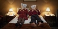 A couple sit in a well lit bedroom with plastic bags over their heads in Bloody Oranges