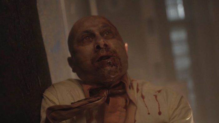 An infected man wearing a dress shirt and tie and covered in blood is seen on the floor in Virus: 32