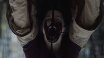 Emily hangs upside down while blood pours down her face in Woodland Grey