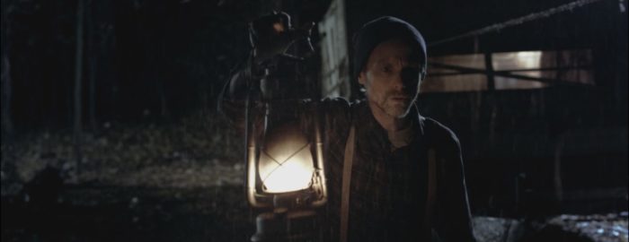 William holds a lantern in the darkened forest of Woodland Grey