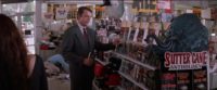 Sam Neill stands in a bookstore. The shelves are full of Sutter Cane titles
