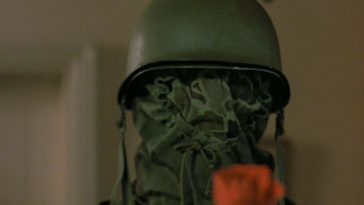 The titular prowler, in helmet, hood, and mesh face mask, holds out a red rose.