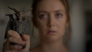 A woman holds up a small figure of a horned creature with wings.
