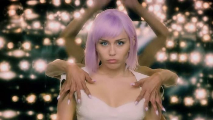 Miley Cyrus stands center surrounded by lights and hands uncomfortably touching her in Black Mirror