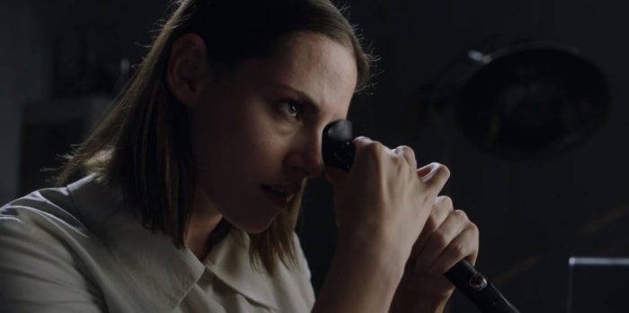 A woman examines something unseen through what looks like a microscope.
