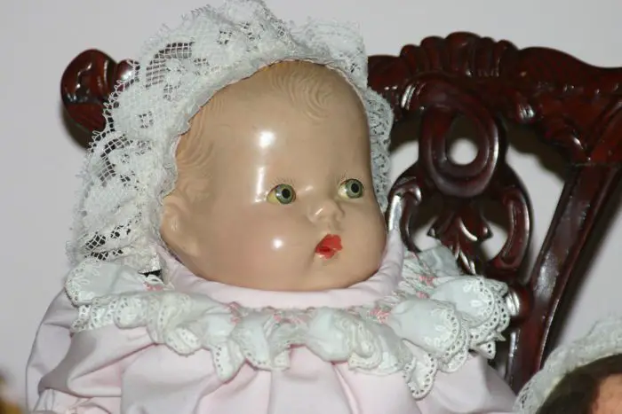 A close up of a baby doll wearing a white lace bonnet.