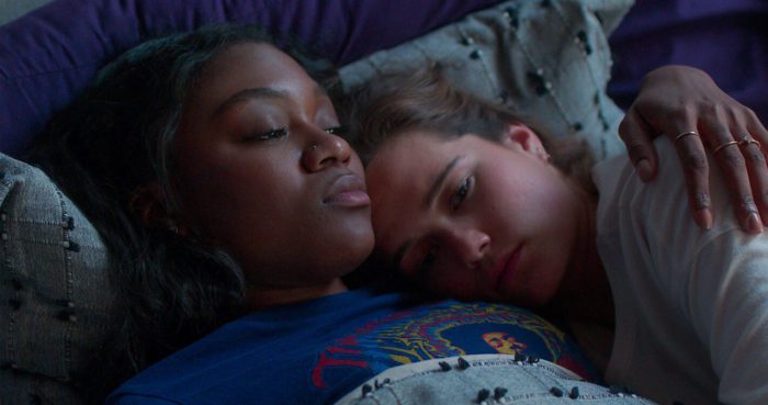 Two young women lay in bed with their arms around each other.