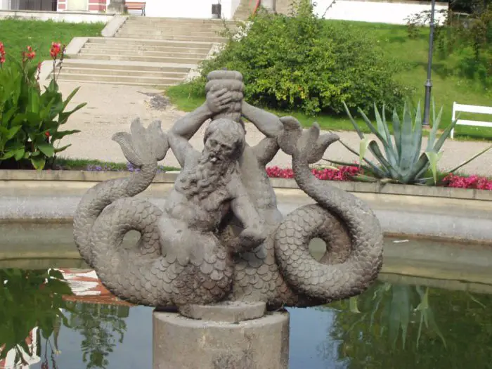 Merman statue sits with its tail coiled holding a chalice up over his head.