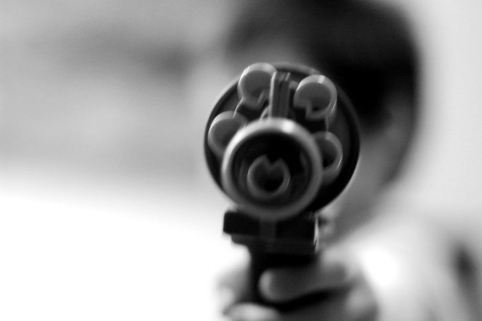 Closeup of a person pointing a gun at the camera.