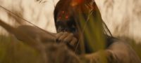 A hunter with a drawn bow hides in the tall grass while a three dotted laser sight is shown on his head in the Prey (2022) teaser