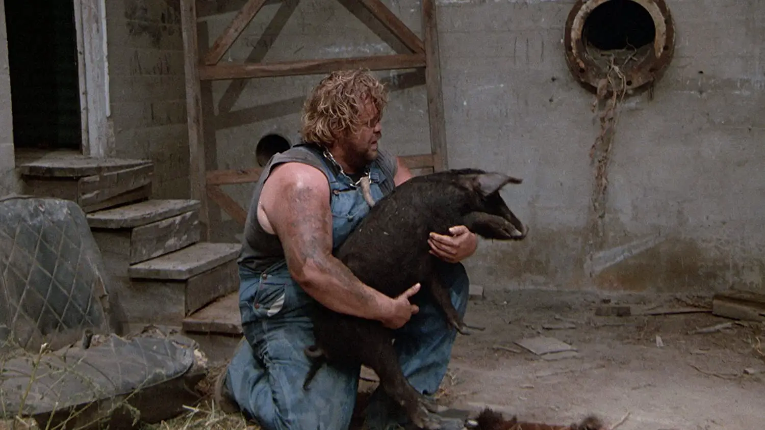 Buddy kneels on the ground, cradling a pig.