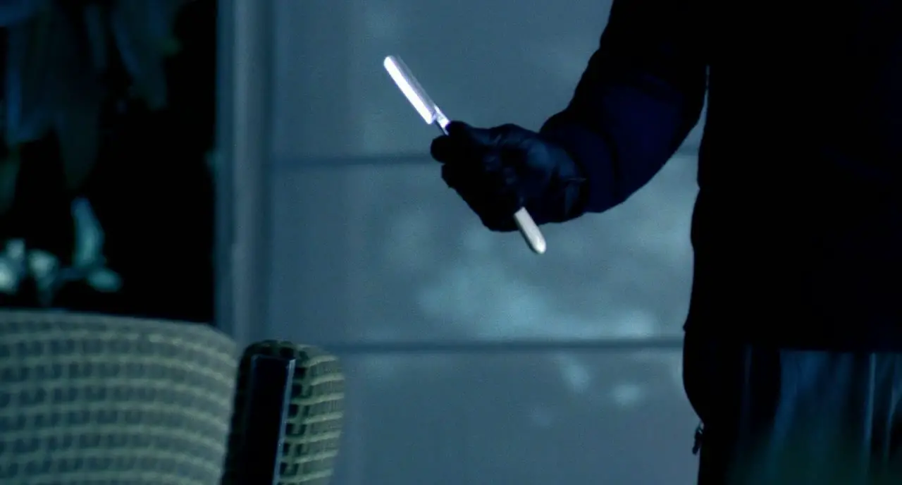 A person in a black shirt and gloves holds out a straight razor.
