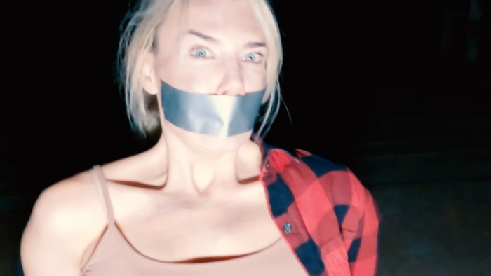 Jenna sits in a chair with duct tape over her mouth looking into the camera in A Town Full of Ghosts