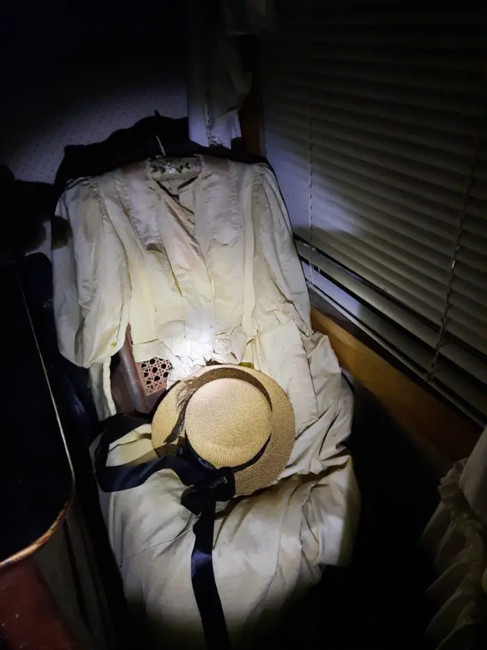 A flashlight illuminates a 1900s dress on an old rocking chair