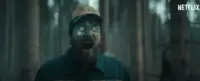 A man with glowing green eyes yells toward the camera in a wooded area in Blasted.