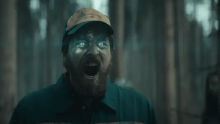 A man with glowing green eyes yells toward the camera in a wooded area in Blasted.