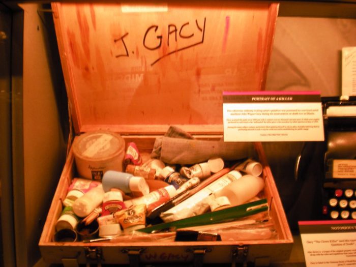 A wooden box open with the name J. Gacy written on the inside of the lid. It's filled with chalk and assorted art supplies.