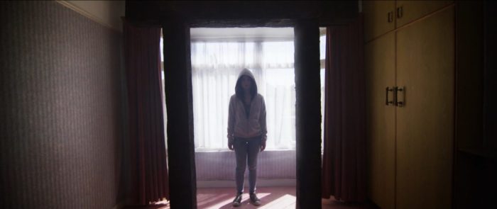 A hooded young girl stands in a doorframe in Gateway