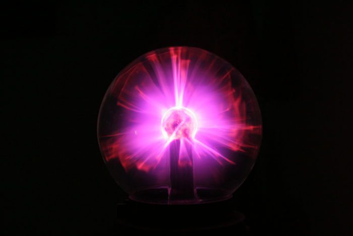 A plasma ball emits a purple glow in the dark.
