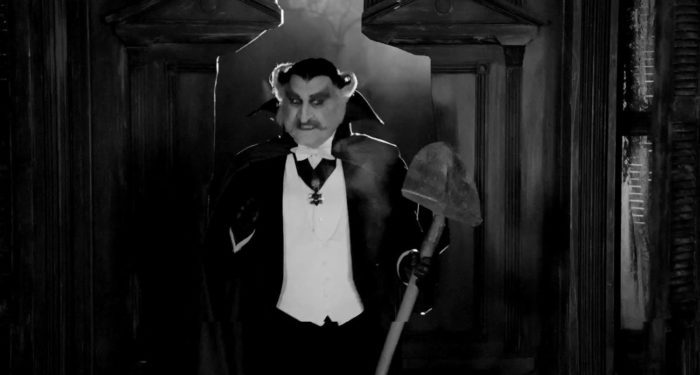 Grandpa makes it through the cutout of Herman in the door with a shovel in The Munsters teaser