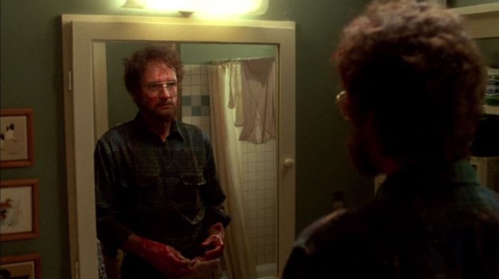 The bloody and bearded Stepfather looks into a bathroom mirror.