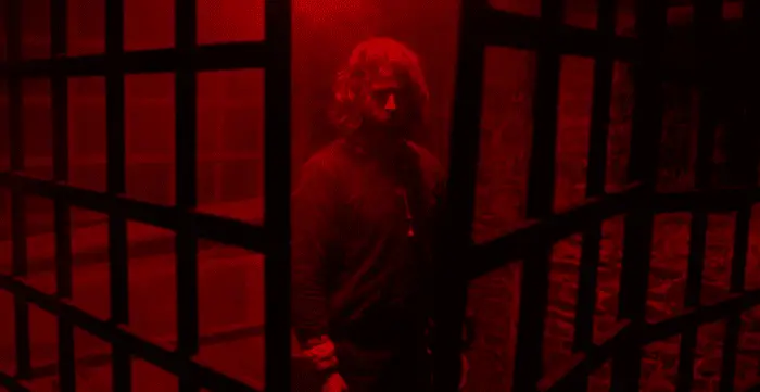 a man illuminated on red light stands in a jail cell