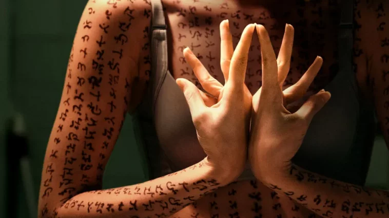 A woman covered in runes, her hands creating a flower shape in prayer gesture