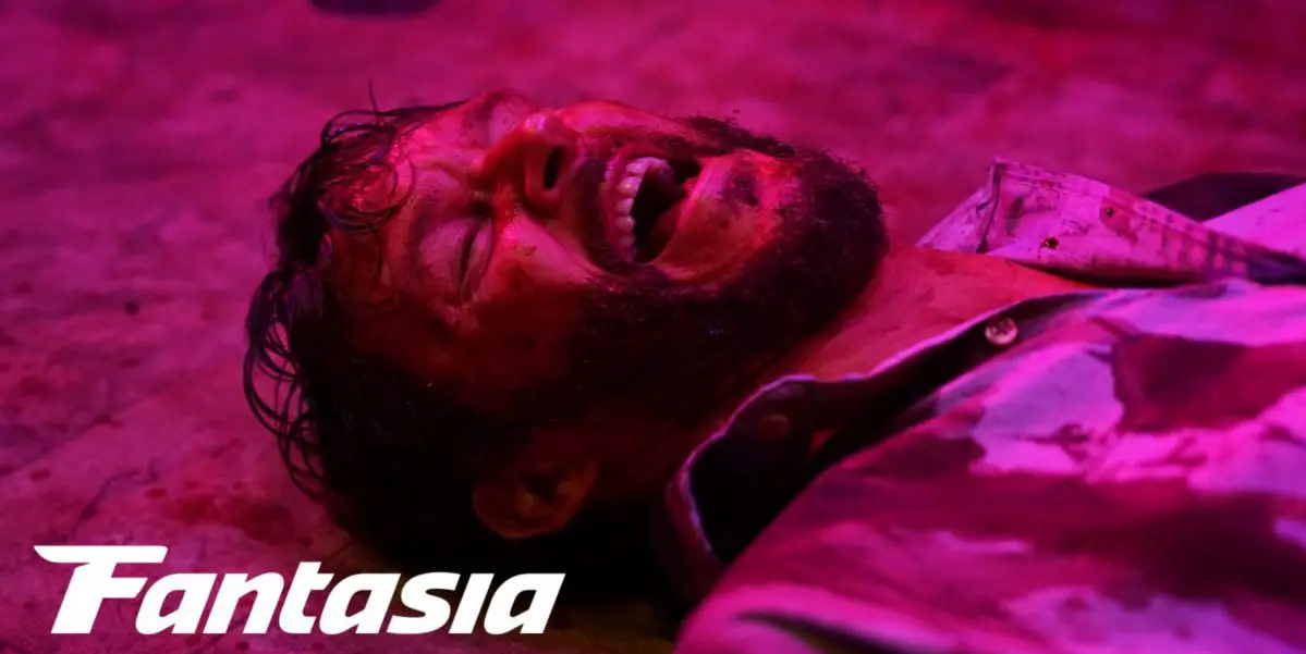 Wes laughs on the floor covered in blood under a magenta light in Glorious