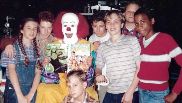 A cast photo shows the young kids gathered around Tim Curry in full Pennywise makeup in Pennywise: The Story of IT